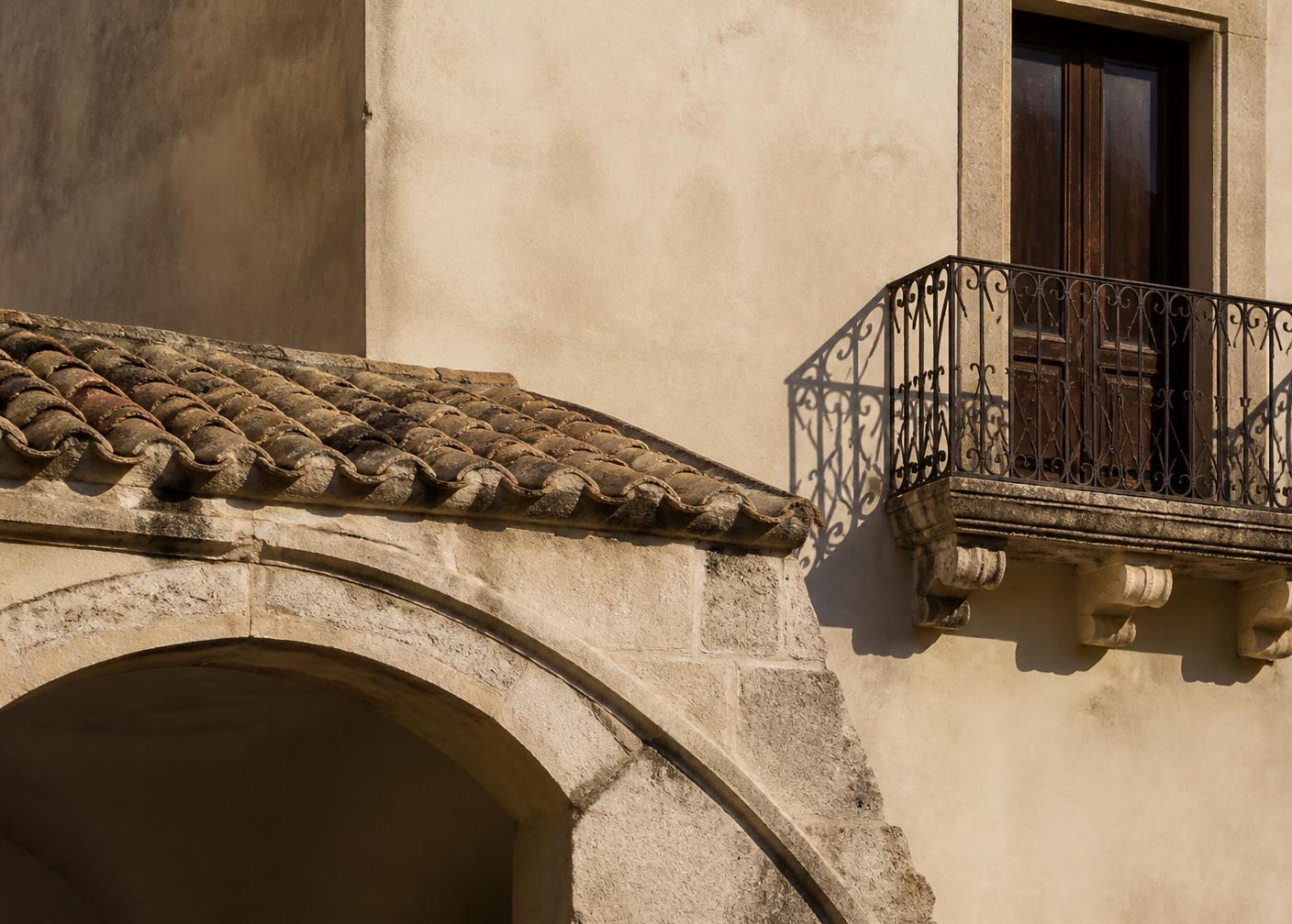Stone arch, terracotta roof tiles and wrought-iron balcony on an Italian facade